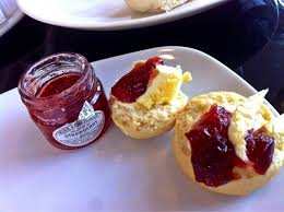two scones with cream and jam little pot of strawberry jam on white plate