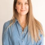 Woman in 40s long straight light brown hair smiling. Denim light blue shirt top two buttons undone