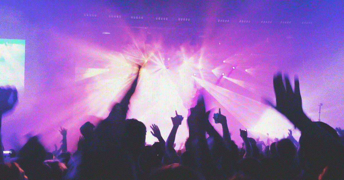 people sihouted with arms up purple and white background of flashing lights