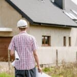 man with checked shirt back to camera white hard hat walking towards house