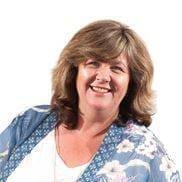 Linda Reynolds headshot. Woman in 50s short light brown wavy hair white top blue and flowers trimmed jacket