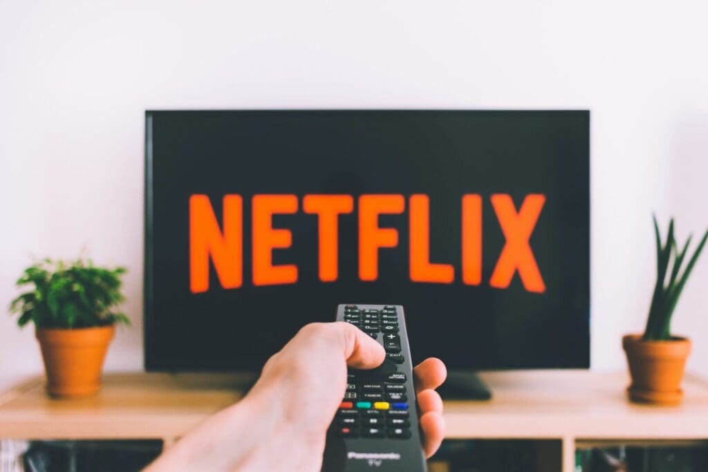 Hand on remote pointing at TV with the word Netflix on it