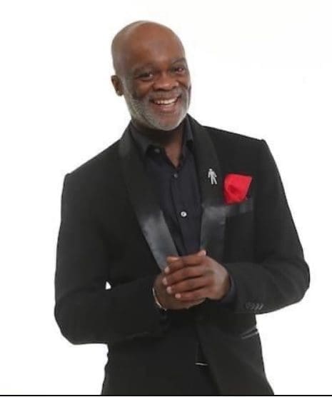 Eddie Nestor waist up smiling in black shirt and jacket red rose