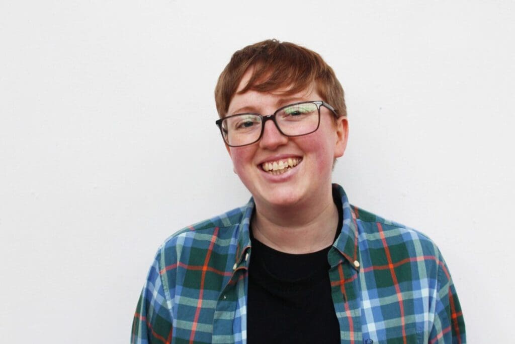 Transgender male headshot with glasses and short hair checked shirt