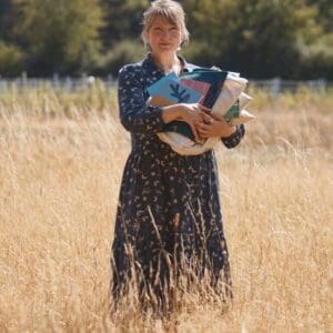 woman in dress in field holding books