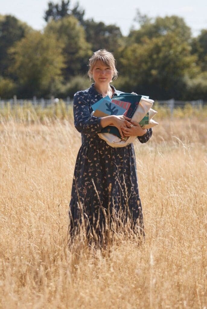woman in dress in field holding books