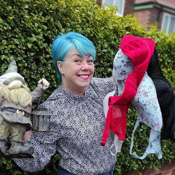 Janine with blue hair holding up bras