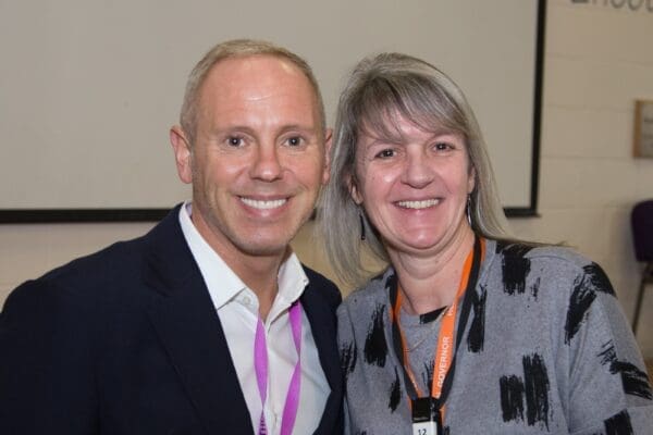 Rob Rinder and Helen Dewdney standing woman grey/blond shoulder length hair gray and bloack top man in blue suit short grey/blond hair