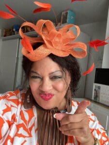 Black woman pointing finger sassy face orange fascinator bows orange and white top