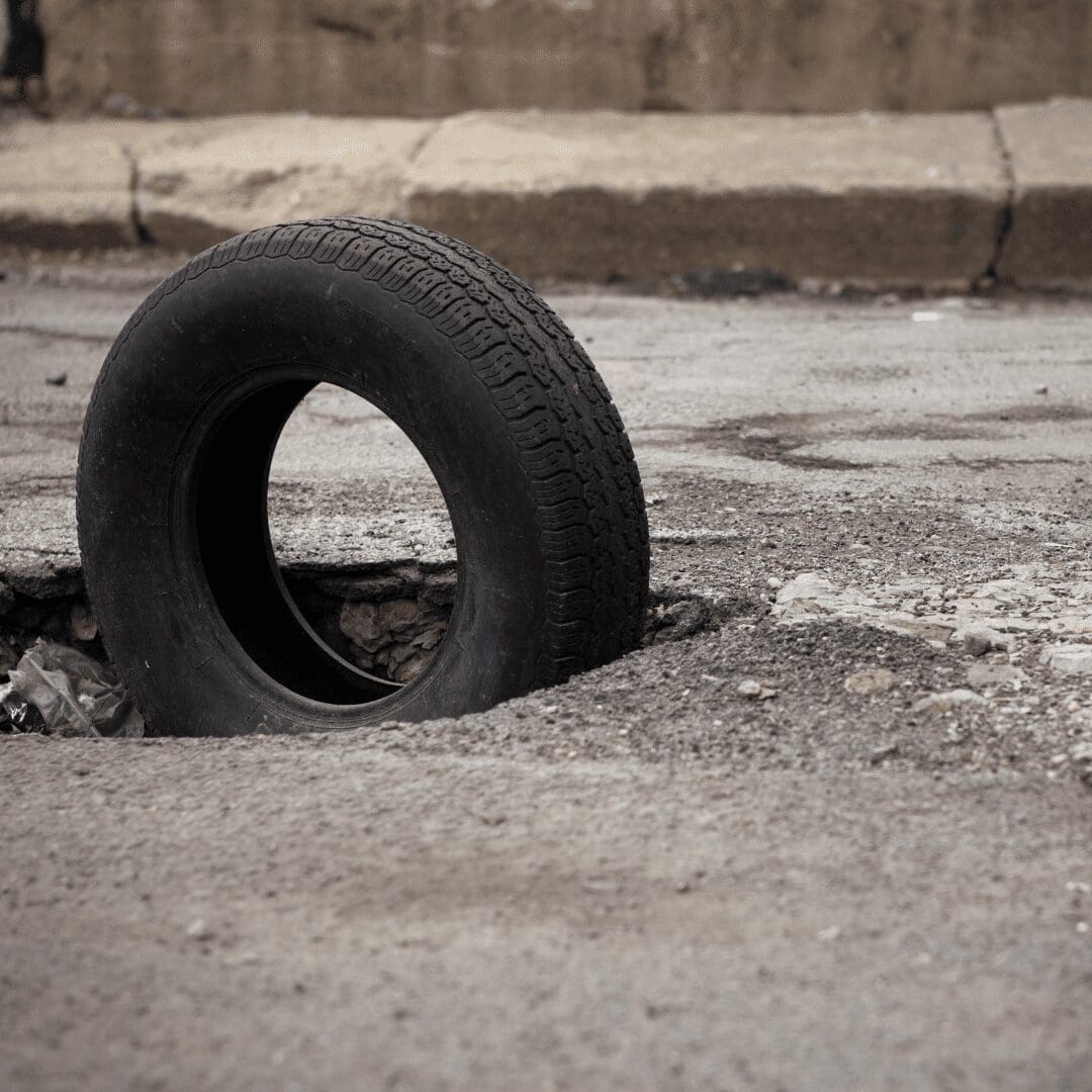 Big pothole in the road with tyre standing up in it