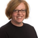 Head shot woman smiling in glasses short ginger/blond hair black top