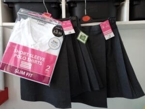 3 black school uniform shirts hanging up with packet of white girls shirts