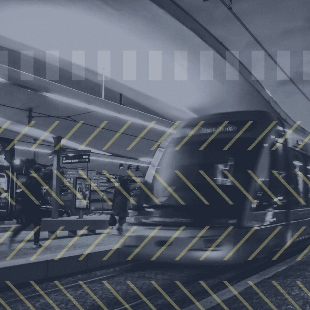 Black and white picture train on platform two people walking 4 lines of yellow zig zag lines