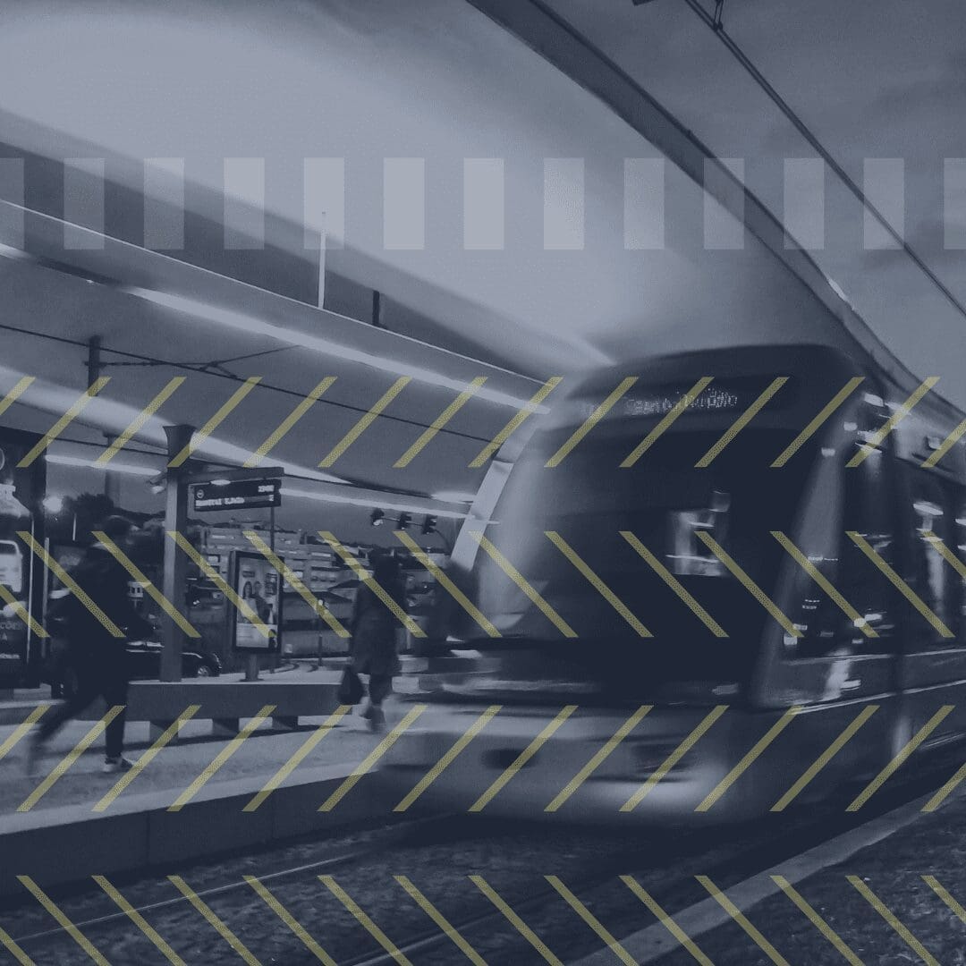 Black and white picture train on platform two people walking 4 lines of yellow zig zag lines