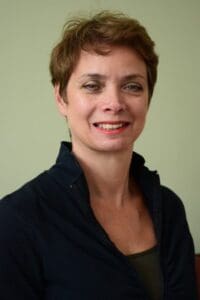 White woman black top high collar cropped brown hair, smiling