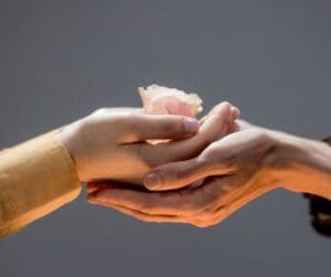 outstretched light brown arm and hand on top of another coming from the left with flower on top hand