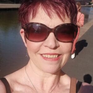 Head shot short red dyed hair brown sunglass woman in 50s black thin straps of top just showing