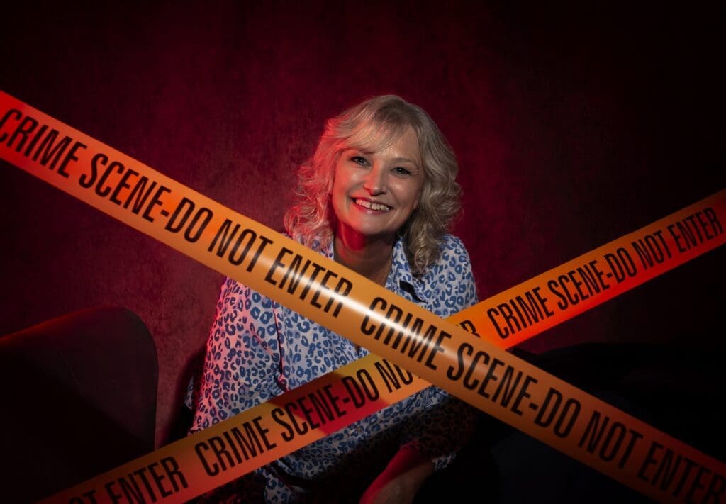 Crime scene tape crossed over in front of white woman smiling blond shoulder length curly hair blue and white spotted top