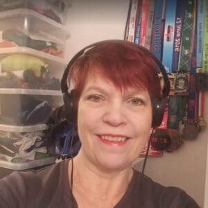 Head shot woman in 50s dyed red hair smiling headphones clear plastic boxes in background