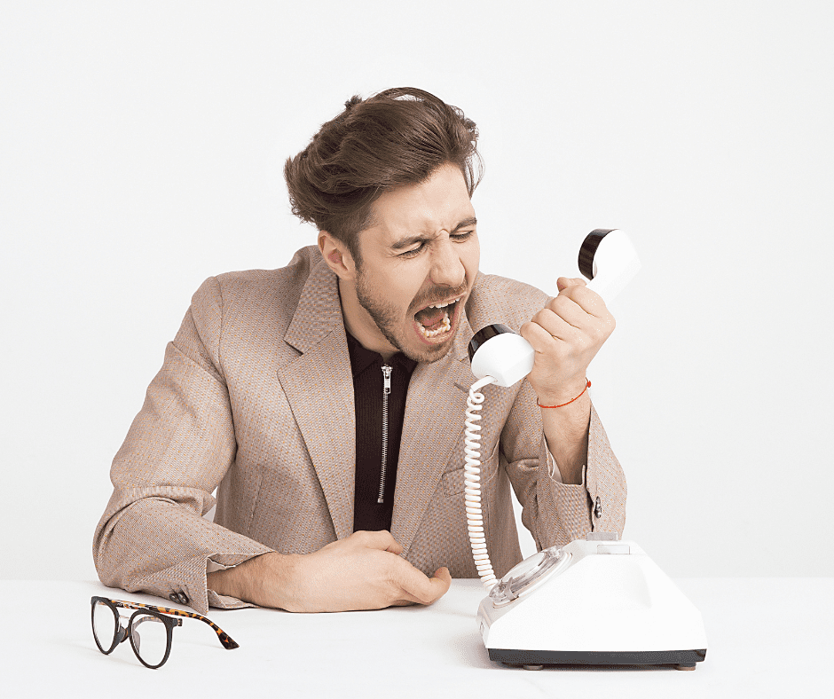 White man in 20s short brown hair, moustache light brown jacked on black top holding receiver of old fashioned white phone and shouting into it