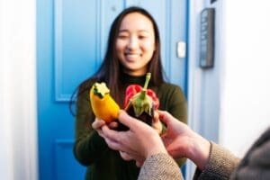 Woman outside blue front door being handed vegetables