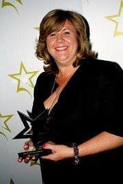 Woman in 50s short shoulder length wavy light brown hair smiling. Black dress head to middle shot. Holding award. Background white with yellow outline stars