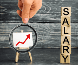 background grey slate building wooden blocks tower letter on each to spell out "salary" top down to left little white rectangle on wooden easel red arrow on the rectangle black circle round the rectangle, white hand thumb on the circle