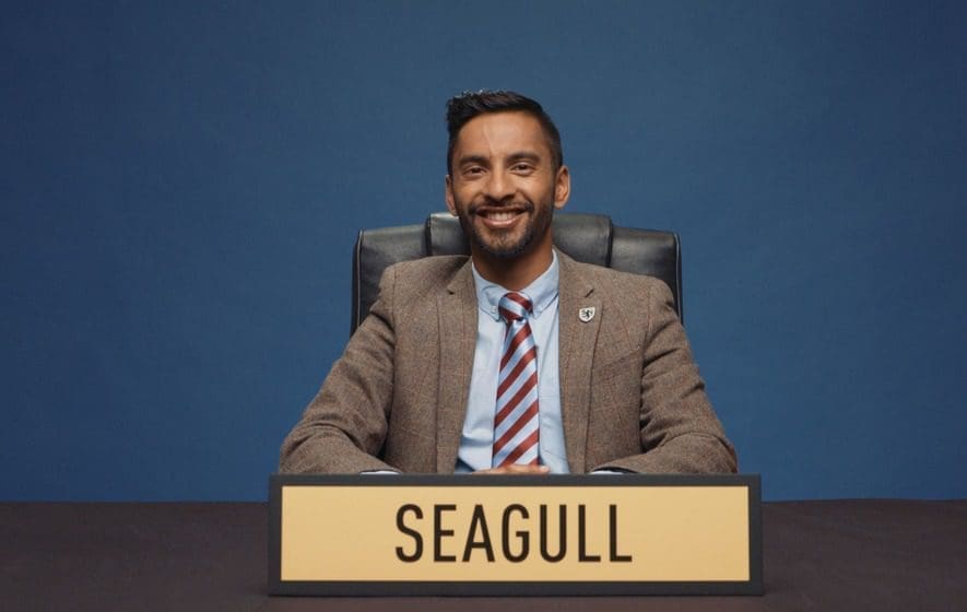 Asian man with bead smiling light brown suit jacket blue shirt red and blue striped tie name SEAGULL in front image from University Challenge