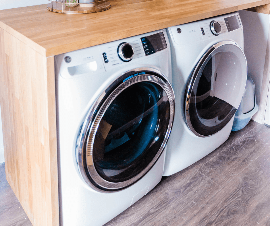2 white washing machines on lino floor encases in wooden top and side