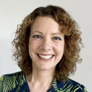 smiling white woman head shot shoulder length tight curly hair green and black shaded stripe top