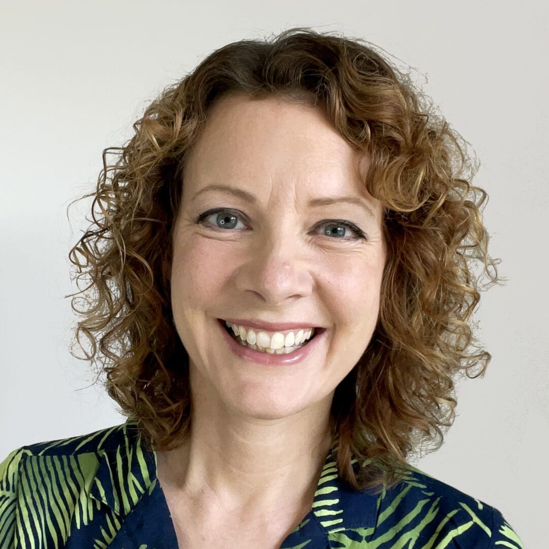 smiling white woman head shot shoulder length tight curly hair green and black shaded stripe top