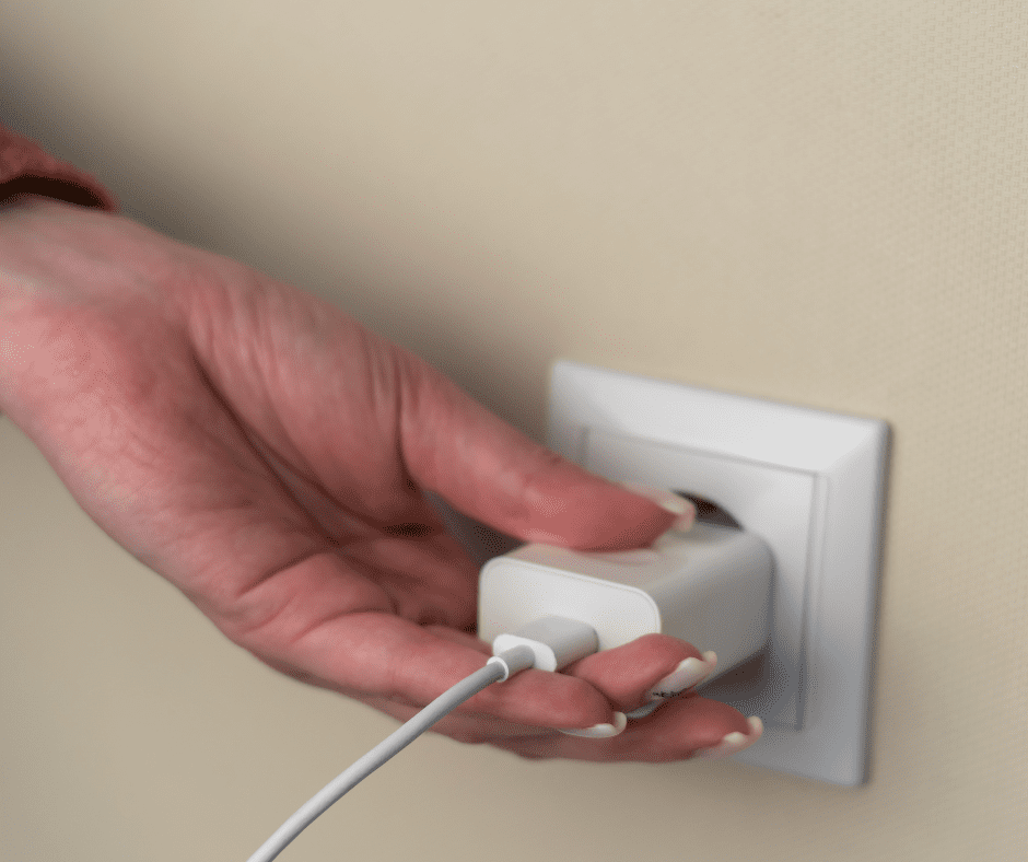 beige wall white socket, white left hand plugging in phone blug into socket
