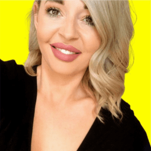 White woman in late 20s wavy blond hair smiling head shot yellow background black v neck top.