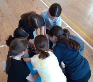 6 children bent over a table hiding what is on the table as heads are all together