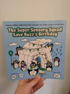 White hand holding a blue book with cartoon penguins