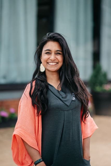 Asian woman in early 30s long black hair smiling at camera dark grey top orange loose top over arms