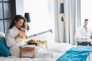 White woman in 30s sitting up in bed with tray over her eating