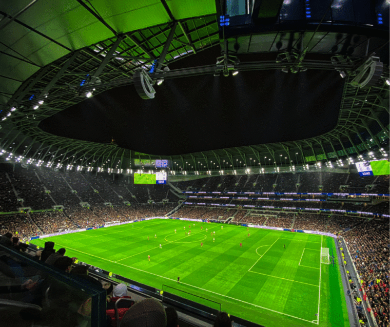 football stadium, whole green pitch people all around full stadium no detail on the people lights above