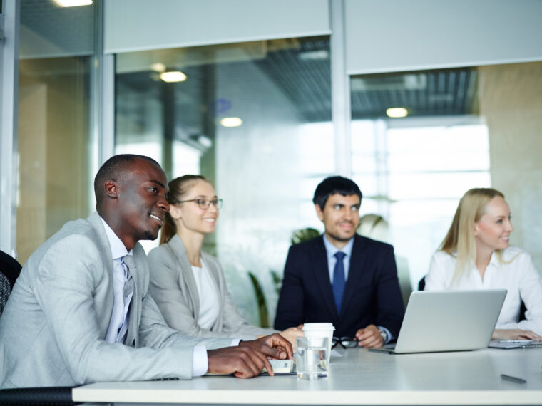 International group of young enthusiastic business people smiling sitting round meeting table in conference room of modern office