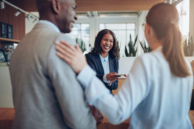 Laughing young African American concierge helping two guests check in while working behind a hotel counter