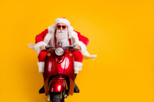 Portrait of serious hipster santa claus in red hat drive his scooter hurry, rider ride to x-mas christmas party wear shirt suspenders isolated over yellow colour background