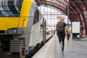 Female tourist with backpack running to the train on railway station platform, travel in Europe. Transportation by european railroads, comfortable tourism and travelling