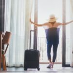 Women with hat on opening the curtains to floor in front of balconyand door in the room looking to outside view. Travel in holidays concept. Vintage tone