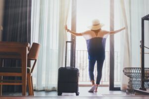 Women with hat on opening the curtains to floor in front of balconyand door in the room looking to outside view. Travel in holidays concept. Vintage tone