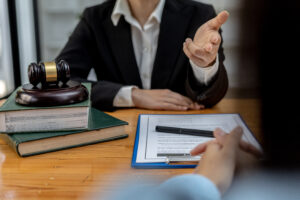 person body no head shot of white person in black jacket and white shirt arm on tabl other outstretched to peron in fromt see arm across table on clipboard with paper and pen
