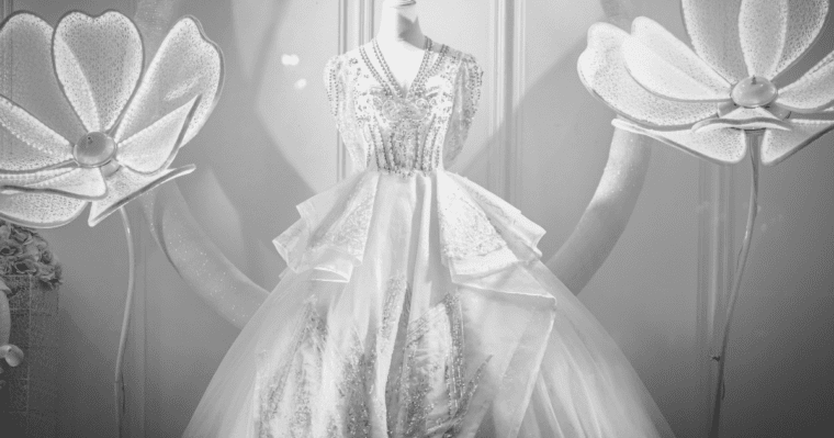 Black and white image big flowers either side of white wedding dress on mannequin with no head