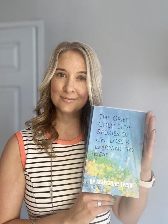White woman long wavy blond hair in early 40s white and black thin stripe t shirt holding a blue covered book and smiling