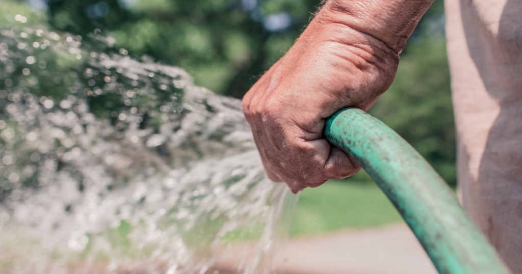 hand holding a green hose with water spraying out
